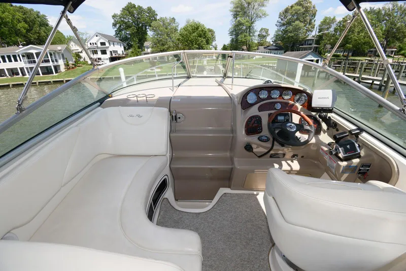 Slide: The Image of 2005 Sea Ray 280 Sundancer cockpit with steering wheel, gauges, and seating, docked by waterfront homes. - 3