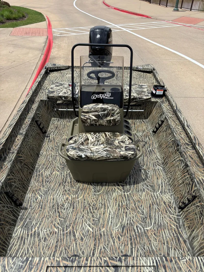 Slide: The Image of 2025 Tracker Grizzly 1860 CC boat with camouflage interior, parked on a paved surface. - 5
