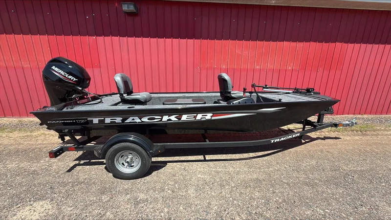 The Image of 2025 Tracker Panfish 17 boat with Mercury engine, parked on trailer, red building background. - 0