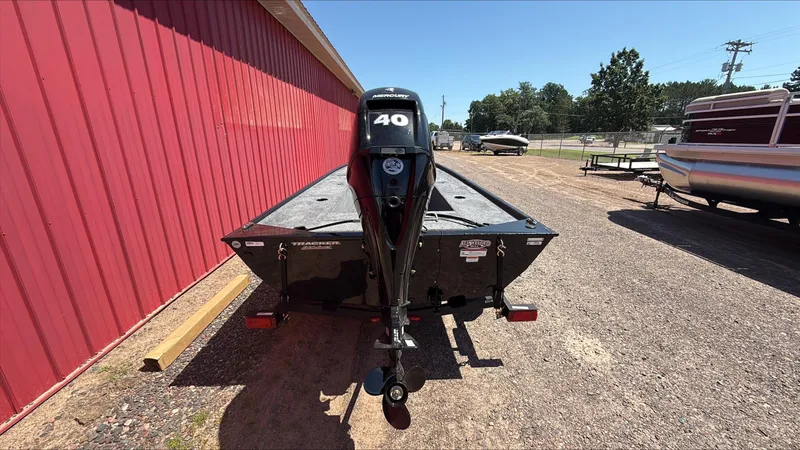 Slide: The Image of 2025 Tracker Panfish 17 boat with 40 HP Mercury engine, parked beside a red building. - 3