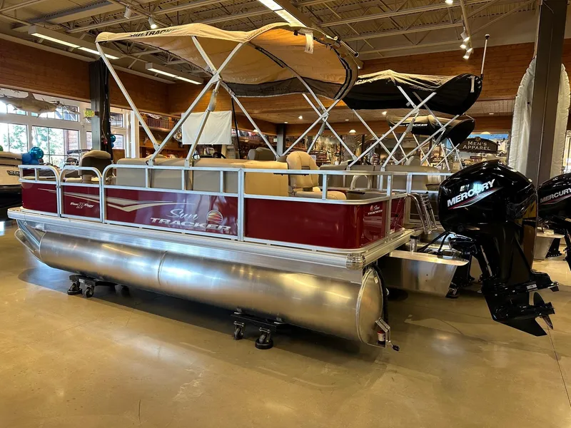 Slide: The Image of 2025 Sun Tracker Bass Buggy 18 DLX pontoon boat displayed indoors with Mercury outboard motor. - 2
