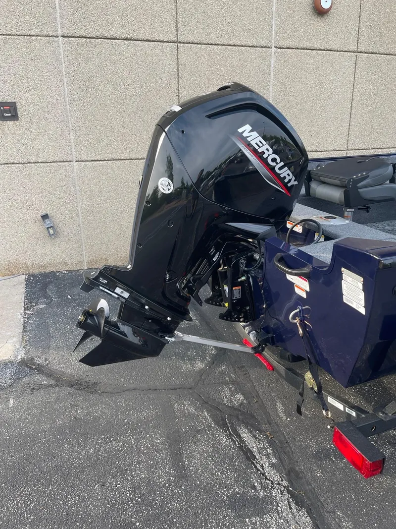 Slide: The Image of 2025 Tracker Pro Guide V-16 SC boat with Mercury outboard motor, parked on pavement. - 2