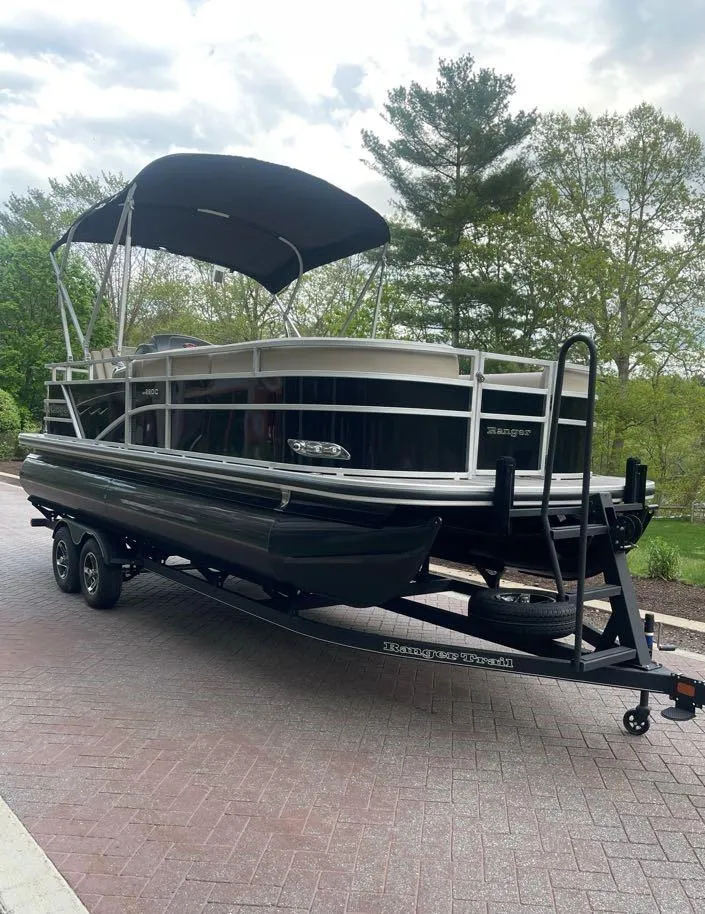 Slide: The Image of 2025 Ranger Reata 220C pontoon boat on trailer, parked outdoors with canopy. - 2