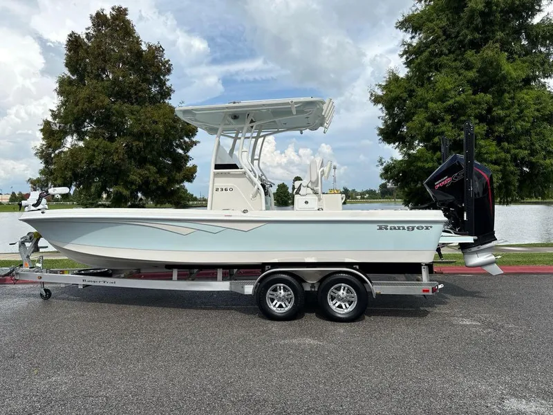 The Image of 2025 Ranger 2360 Bay boat on trailer by a lake, under cloudy sky. - 0