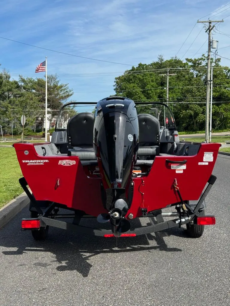 Slide: The Image of 2025 Tracker Pro Guide V-16 WT boat, red exterior, parked on a road with trees and flag. - 2