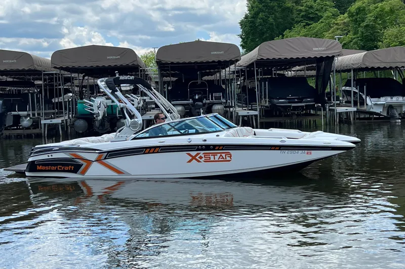 Slide: The Image of 2013 MasterCraft XStar boat on a calm lake near covered docks. - 0