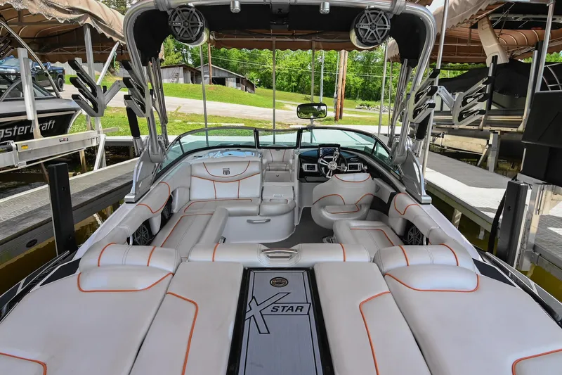 Slide: The Image of 2013 MasterCraft XStar boat interior with white seating and orange accents, docked in a marina. - 11