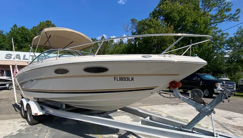 The Image of 2000 Sea Ray 230 boat on trailer, parked outdoors, with trees in the background. - 0