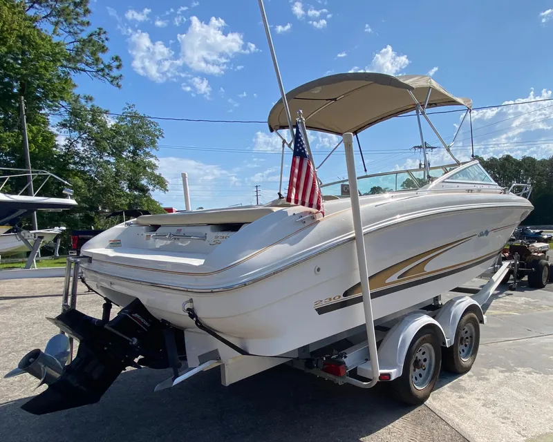 Slide: The Image of 2000 Sea Ray 230 boat on trailer with canopy and American flag, parked outdoors. - 2