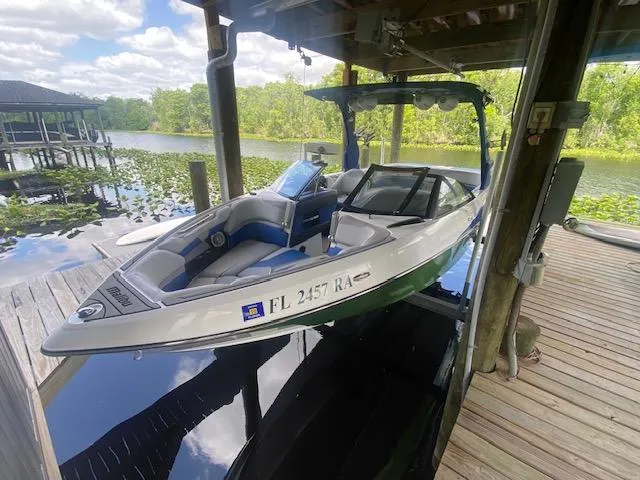 Slide: The Image of 2016 Malibu Wakesetter 25 LSV boat docked on a serene lake under a wooden shelter. - 5
