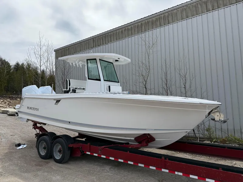 Slide: The Image of 2025 Blackfin 252 CC boat on trailer, parked outdoors near a metal building. - 3