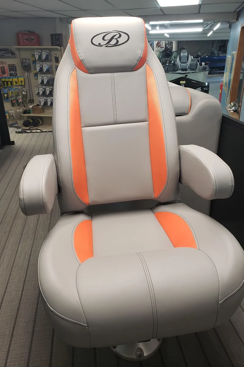 Slide: The Image of 2025 Bentley Pontoons Legacy Navigator captain's chair with orange accents in showroom. - 4
