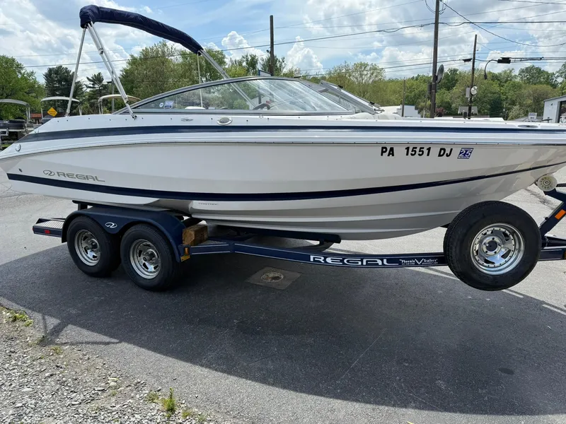 Slide: The Image of 2012 Regal 2000 Bowrider boat on trailer, parked outdoors under a partly cloudy sky. - 6