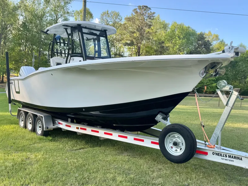 Slide: The Image of 2024 Tidewater 292 CC Adventure boat on trailer, parked on grass with trees in background. - 5