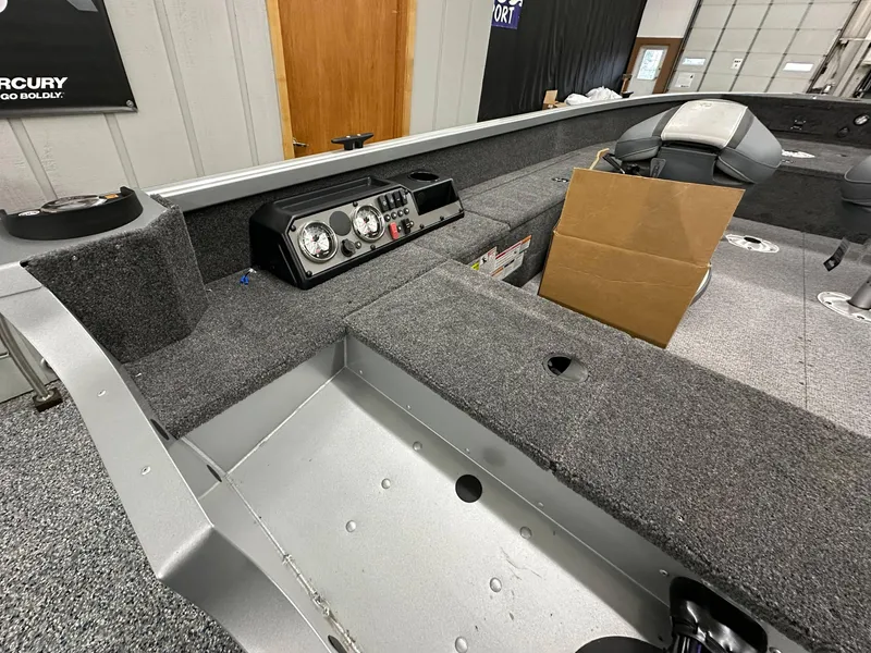 Slide: The Image of 2024 Alumacraft Classic 165 Tiller boat interior with carpeted deck and cardboard box. - 15