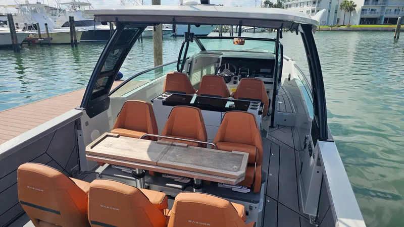 Slide: The Image of 2023 Saxdor 320 GTO boat interior with orange seating and wooden table, docked at marina. - 11