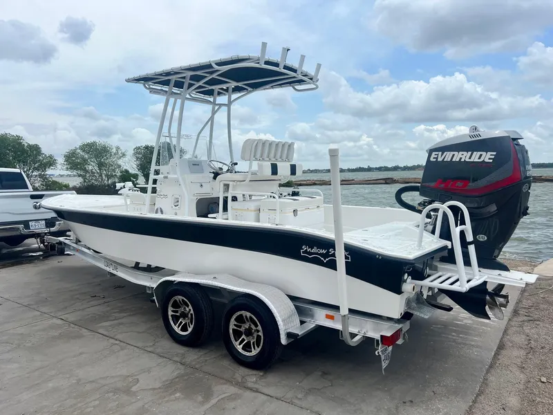 Slide: The Image of 2015 Shallow Sport 24 Modified V boat on trailer with Evinrude engine, docked by a lake. - 2