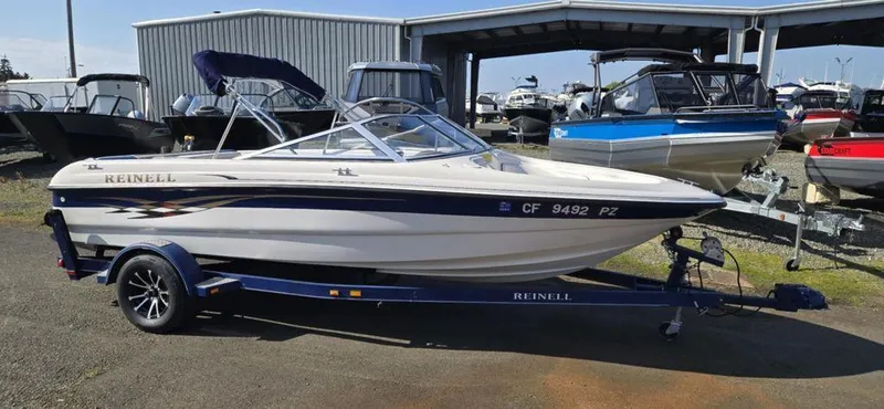 Slide: The Image of 2003 Reinell 185 boat on trailer in marina, surrounded by other boats. - 0