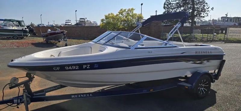 Slide: The Image of 2003 Reinell 185 boat on trailer, parked outdoors, with blue and white design. - 6