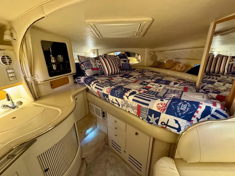 Slide: The Image of Interior of 2000 Sea Ray 310 Sundancer with nautical-themed bedding and compact kitchenette. - 26
