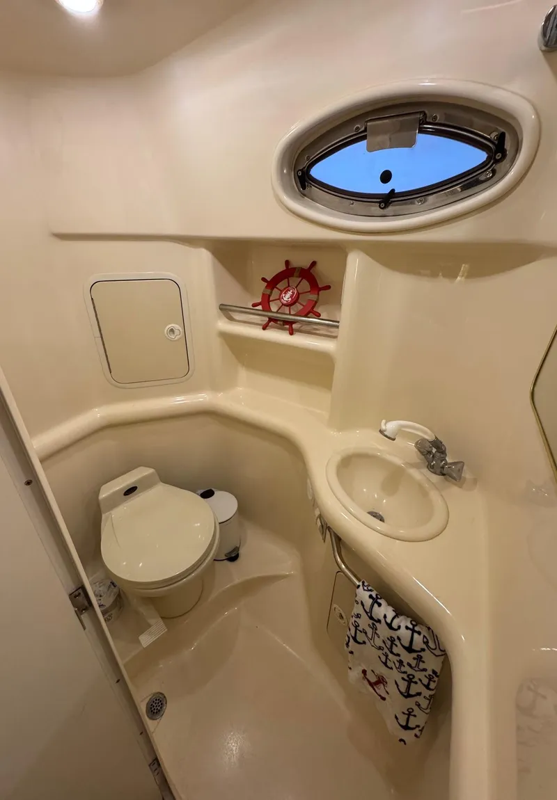 Slide: The Image of 2000 Sea Ray 310 Sundancer bathroom with porthole, sink, and toilet. Nautical-themed decor. - 36