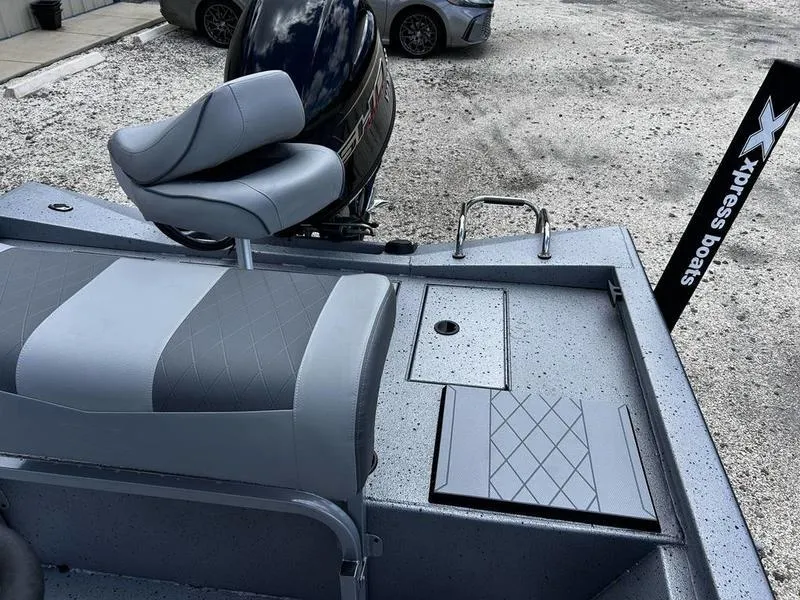 Slide: The Image of 2025 Xpress H190B boat interior with seating and motor, parked on gravel. - 6