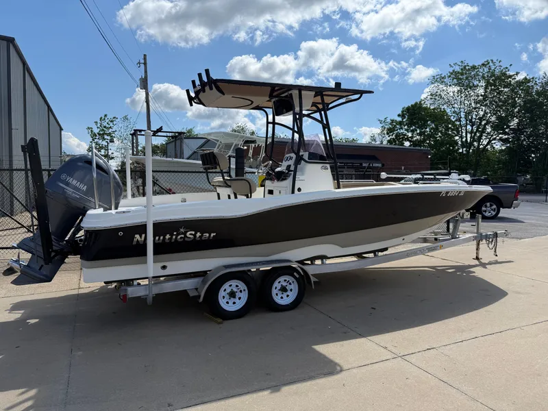 Slide: The Image of 2019 NauticStar 231 Hybrid boat on trailer, parked outdoors under a partly cloudy sky. - 5