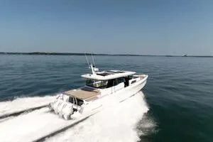 Slide: The Image of 2024 Axopar 45 XC Cross Cabin cruising on calm waters near a lush island. - 2