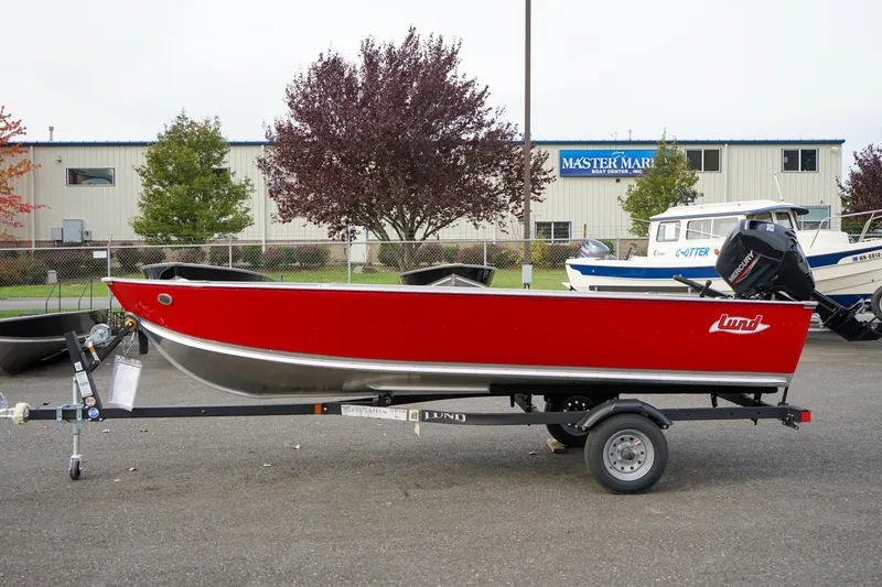 Slide: The Image of 2025 Lund 1600 Fury Tiller boat in red on a trailer, parked outdoors. - 1