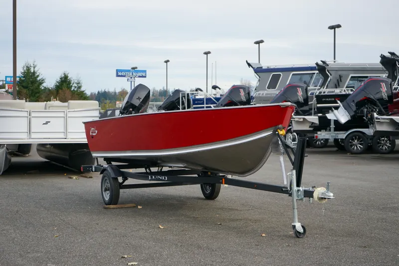Slide: The Image of 2025 Lund 1600 Fury Tiller boat in red on a trailer, parked outdoors. - 12