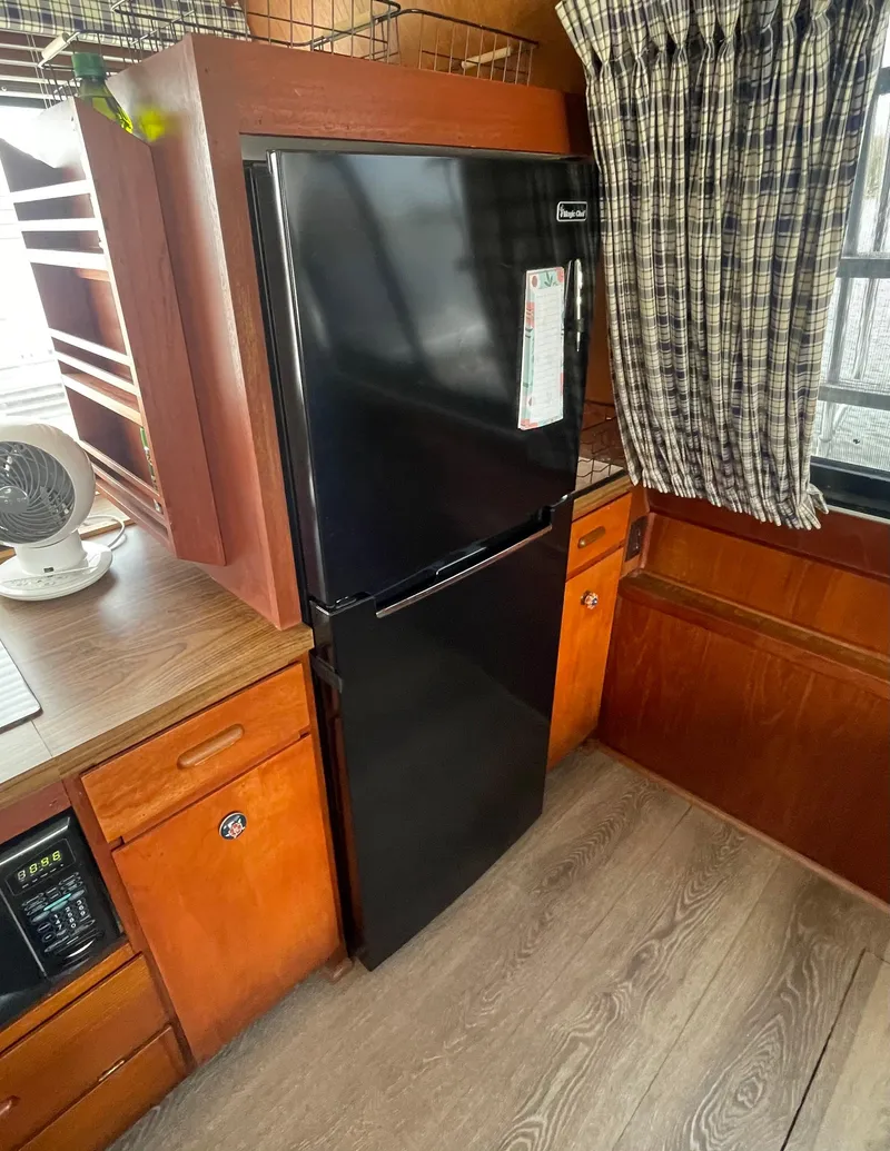 Slide: The Image of Black refrigerator in 1984 Bluewater 42 Coastal Cruiser kitchen with wood cabinetry and plaid curtains. - 41