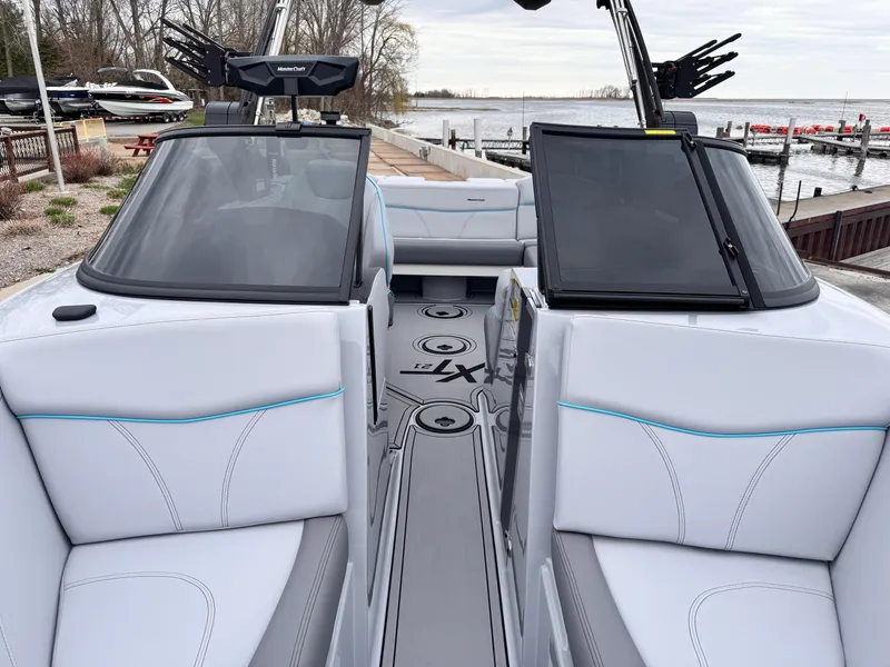 Slide: The Image of 2022 MasterCraft XT21 boat interior with sleek seating and modern dashboard, docked by a lake. - 10