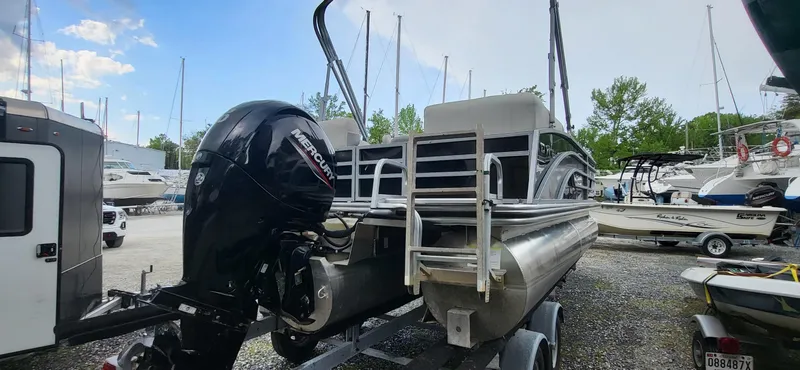 Slide: The Image of 2022 Lowe SS 210 pontoon boat on trailer, parked in marina with other boats. - 10