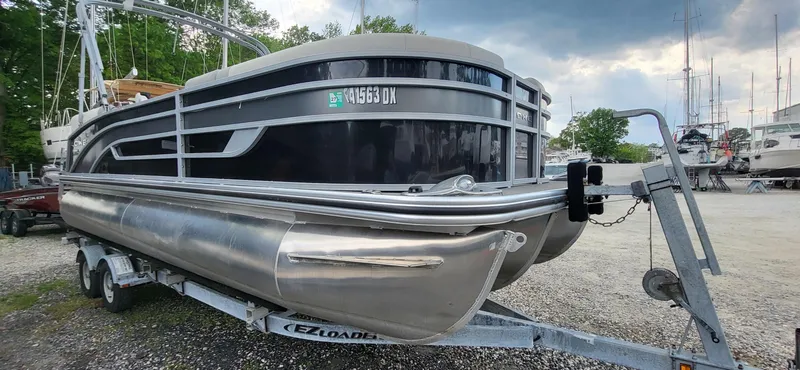 Slide: The Image of 2022 Lowe SS 210 pontoon boat on trailer, parked outdoors under cloudy sky. - 11