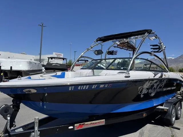 Slide: The Image of 2008 Nautique 230 Team Edition boat on trailer, blue and black design, sunny day. - 3