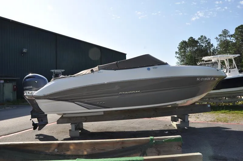Slide: The Image of 2018 Stingray 214 LR boat on display, parked outdoors near a warehouse. - 5
