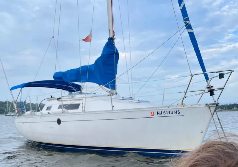 Slide: The Image of 1990 Beneteau First 285 sailboat with blue sail cover on calm water. - 8