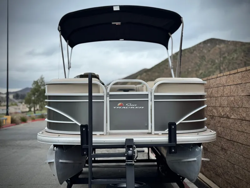 Slide: The Image of 2023 Sun Tracker Party Barge 20 DLX pontoon boat on trailer, parked near mountains. - 2