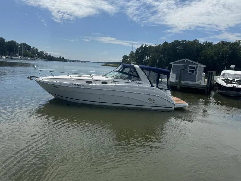 Slide: The Image of 2004 Rinker 342 Fiesta Vee boat docked on a calm river under a partly cloudy sky. - 1
