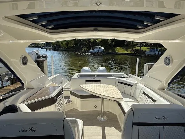 Slide: The Image of 2018 Sea Ray SLX 310 boat interior with seating and table, docked by a scenic waterfront. - 4