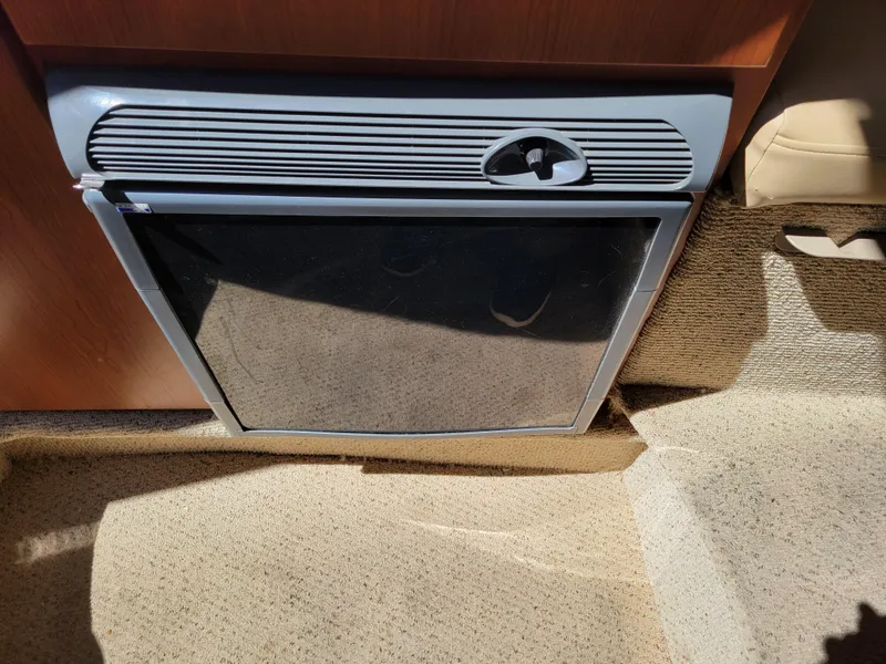 Slide: The Image of 2005 Bayliner 265 interior with built-in mini fridge, beige carpet, and wooden cabinetry. - 21