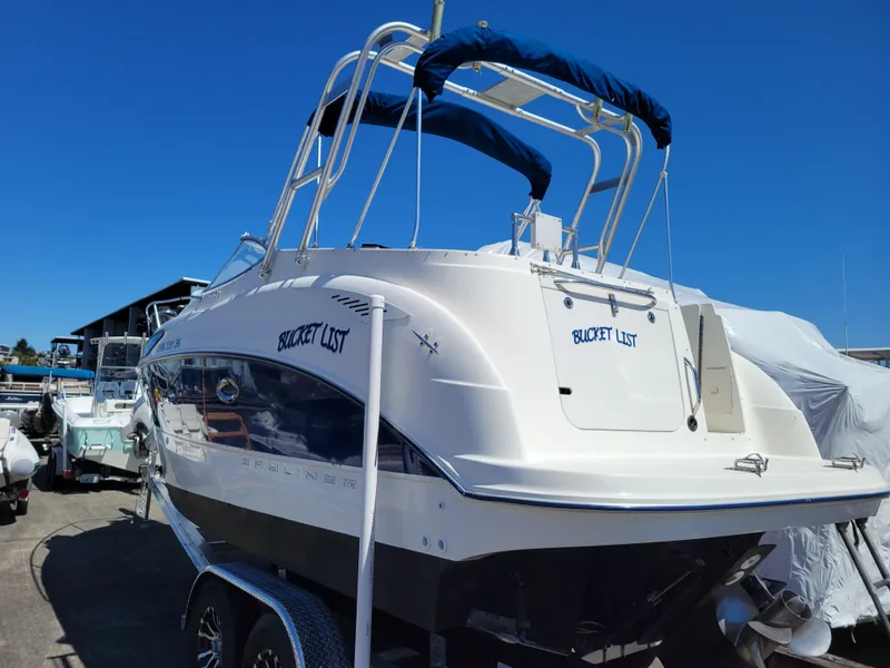 Slide: The Image of 2005 Bayliner 265 boat on trailer, named "Bucket List," under clear blue sky. - 3