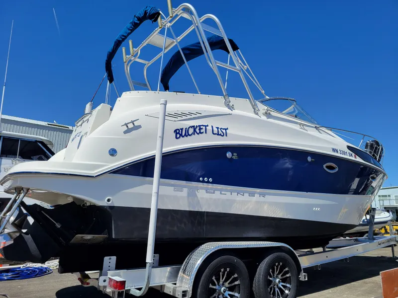 Slide: The Image of 2005 Bayliner 265 boat named "Bucket List" on a trailer under clear blue sky. - 5