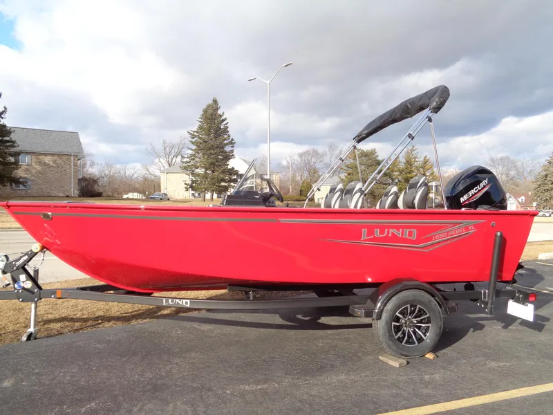 Slide: The Image of 2025 Lund 1650 Rebel XL SS boat in vibrant red on a trailer, parked outdoors. - 4
