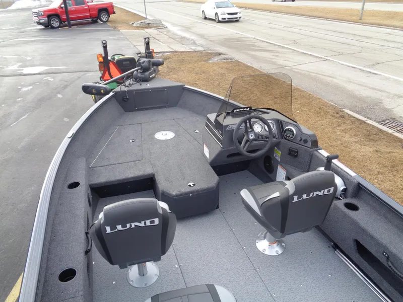 Slide: The Image of 2025 Lund 1775 Adventure SS boat interior with seating and steering console, parked near road. - 13