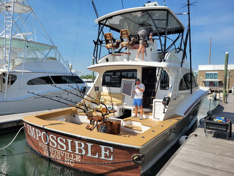Slide: The Image of 2024 Matthews 62 Sport Fish boat docked, featuring fishing gear and two people on board. - 27