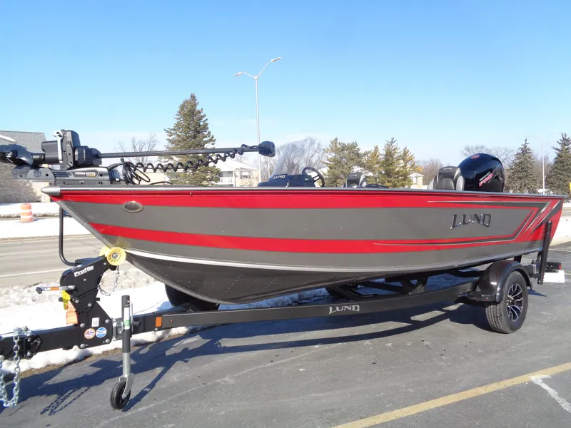 The Image of 2025 Lund 1875 Impact XS SS boat on trailer, red and gray design, parked outdoors. - 0