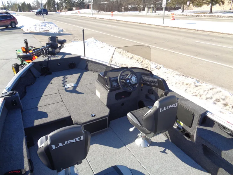 Slide: The Image of 2025 Lund 1875 Impact XS SS boat interior with steering console and seating on a snowy roadside. - 20