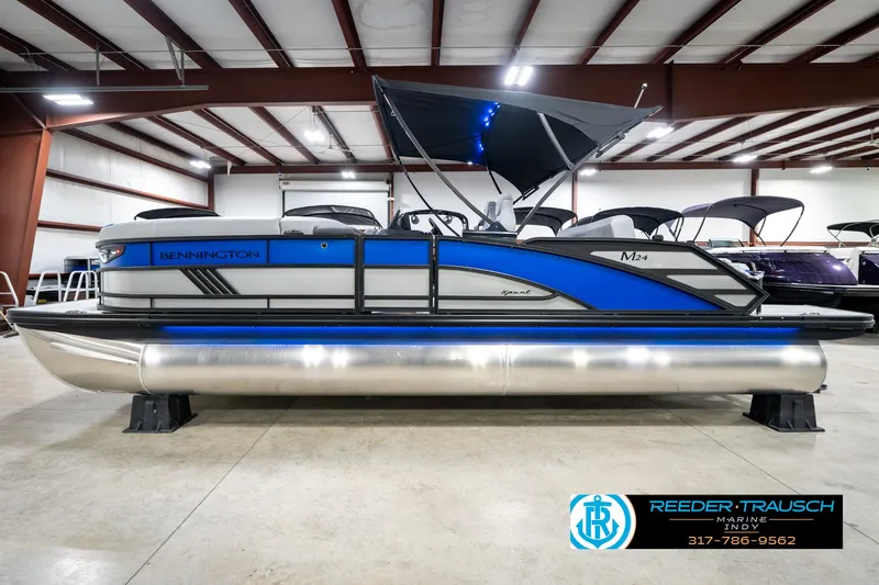 Slide: The Image of 2025 Bennington 24 MSB pontoon boat in showroom with blue accents and canopy. - 11