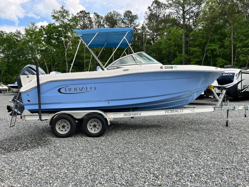 Slide: The Image of 2024 Robalo R207 Dual Console boat on trailer, blue hull, parked outdoors. - 23